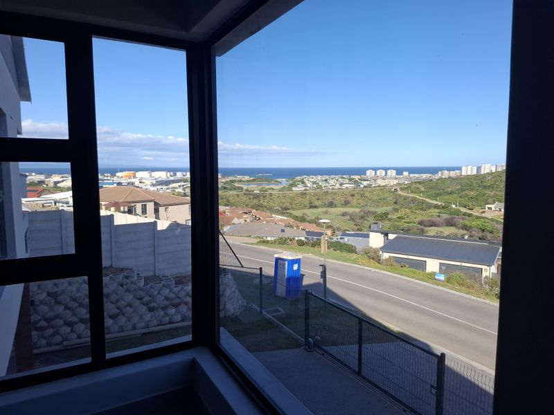 A clear elevated view of the surrounding neighbourhood and coastline captured through large modern aluminium-framed windows.