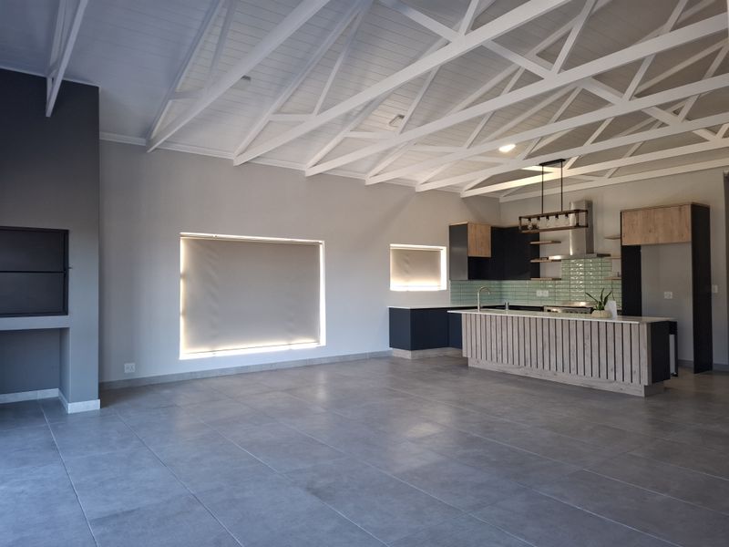 Spacious open-plan living area featuring high vaulted ceilings with exposed trusses, a modern kitchen with island, and a built-in fireplace.