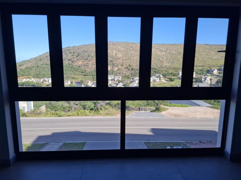 A clear view of the surrounding neighbourhood and hillside landscape captured through a large, modern aluminium-framed window.