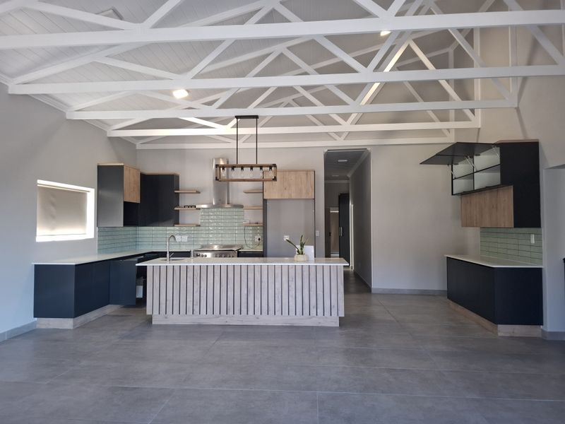 Modern open-plan kitchen featuring a central island, sleek cabinetry, tiled backsplash, and striking exposed white roof trusses in a spacious, well-lit area.
