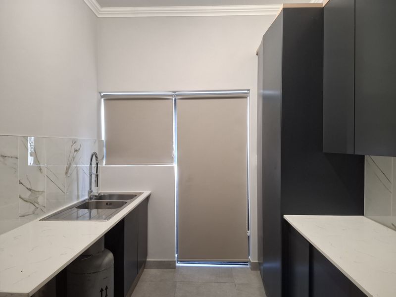A modern, clean scullery featuring dark cabinetry, white quartz countertops, marble-look splashback tiles, and a double basin sink with a gooseneck mixer tap.