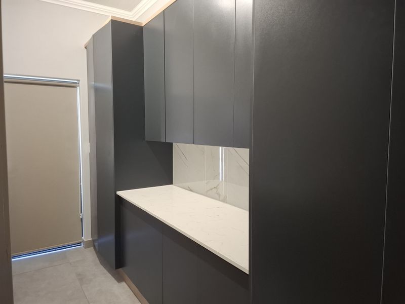 A modern scullery featuring sleek dark cabinetry, a stone countertop, and a marble-look splashback, providing a clean and functional prep or utility space.