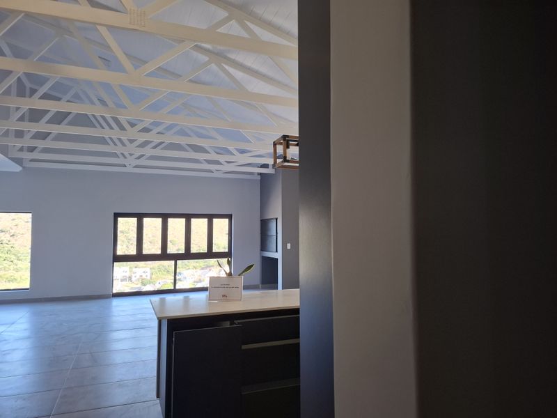 Spacious open-plan living area featuring a vaulted ceiling with exposed white trusses, modern kitchen island, built-in fireplace, and large windows with scenic views.