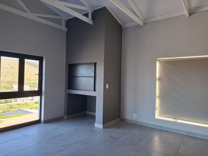 Spacious living area featuring high ceilings with exposed white trusses, modern grey floor tiles, and a built-in fireplace with scenic exterior views.