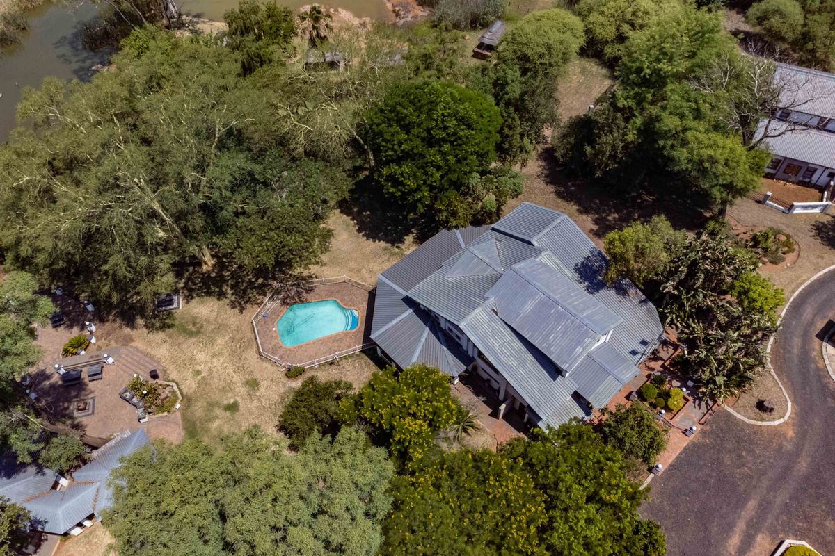 Aerial view of a farm property featuring a large residence with a metal roof, a swimming pool, and extensive landscaped grounds.