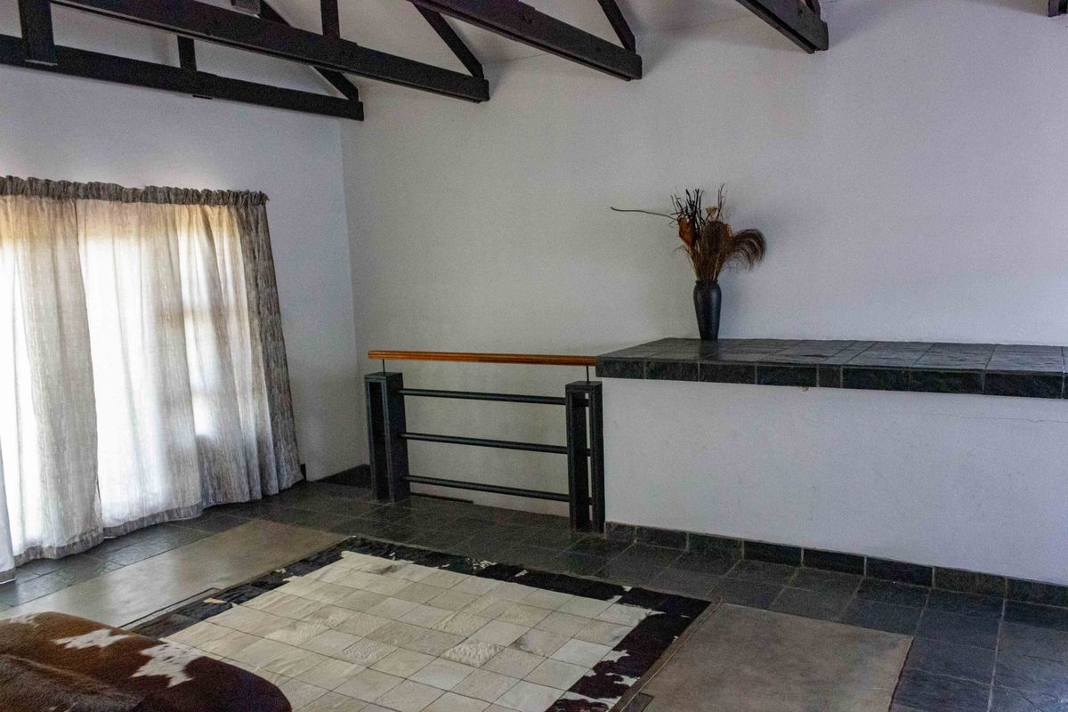 Spacious living area featuring exposed timber roof trusses, dark tiled flooring, and a built-in tiled counter with a metal and wood staircase railing.