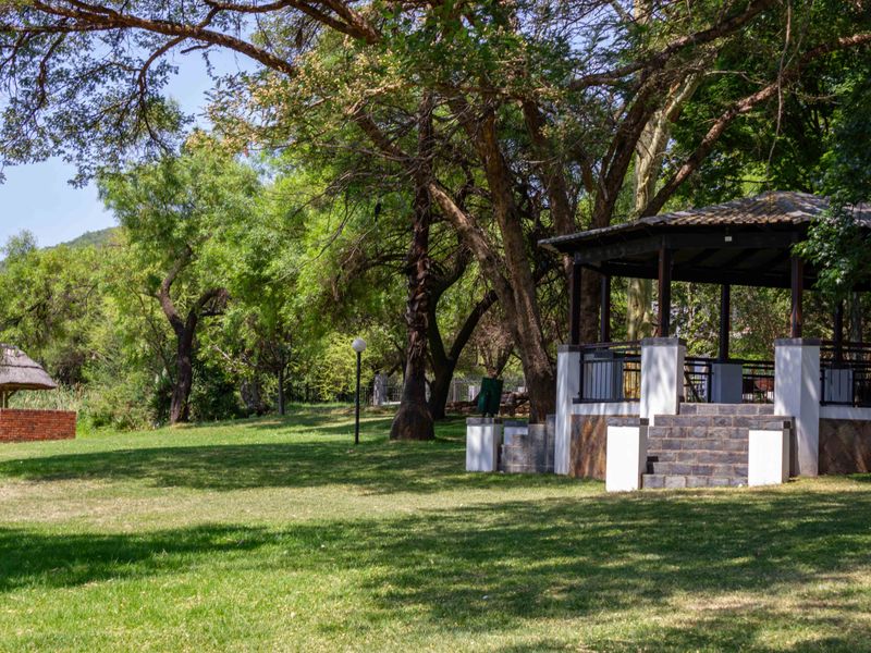 Spacious farm garden featuring a covered gazebo with stone detailing, a brick braai area, and established trees providing a serene outdoor setting.