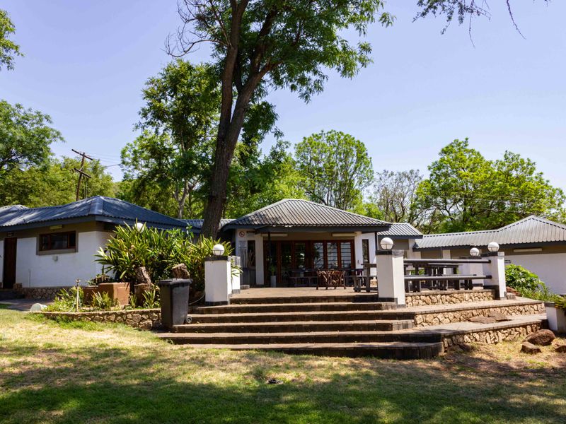 Rear view of the farm property featuring a raised paved patio with stone retaining walls, concrete stairs, and surrounding garden area.
