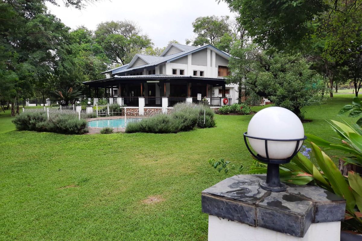 Rear view of the farmhouse featuring a covered patio, swimming pool, and well-maintained garden area with mature trees.