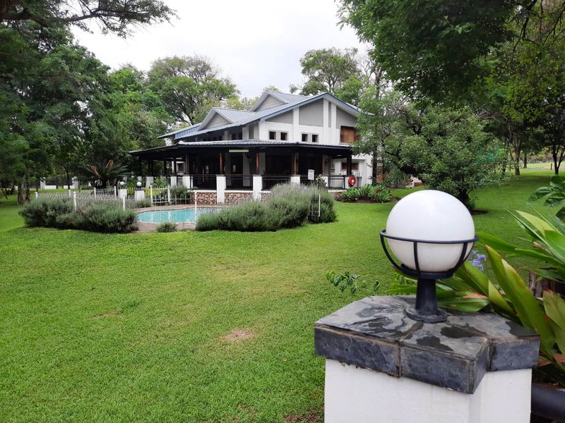 Rear view of the farmhouse featuring a covered patio, swimming pool, and well-maintained garden area with mature trees.