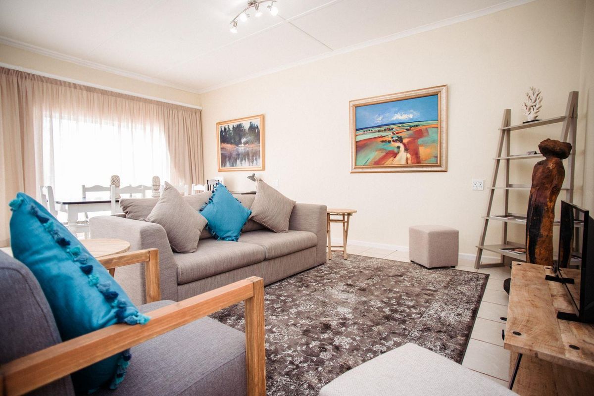 A comfortable living room featuring tiled flooring, neutral walls, and large windows with curtains, providing a bright and inviting space for relaxation.