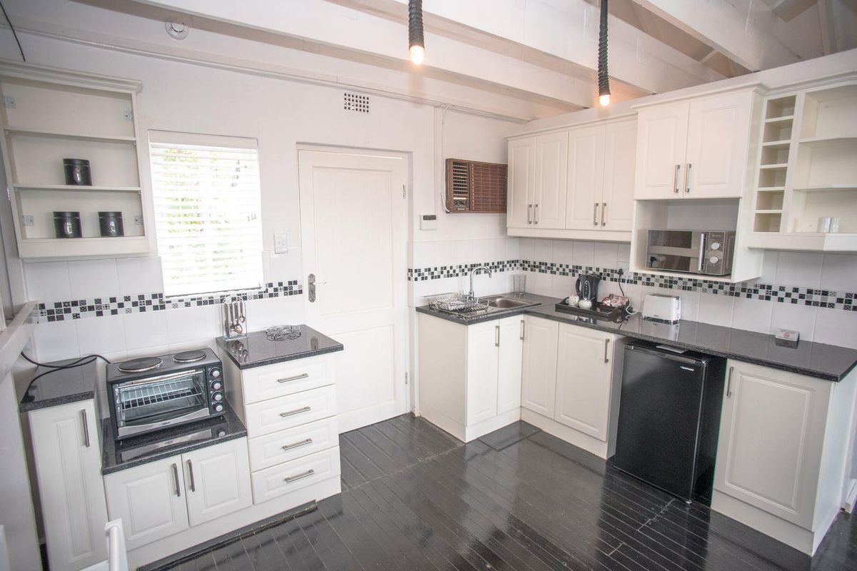 A compact kitchen featuring white cabinetry, dark granite countertops, a tiled backsplash, and exposed ceiling beams with pendant lighting.