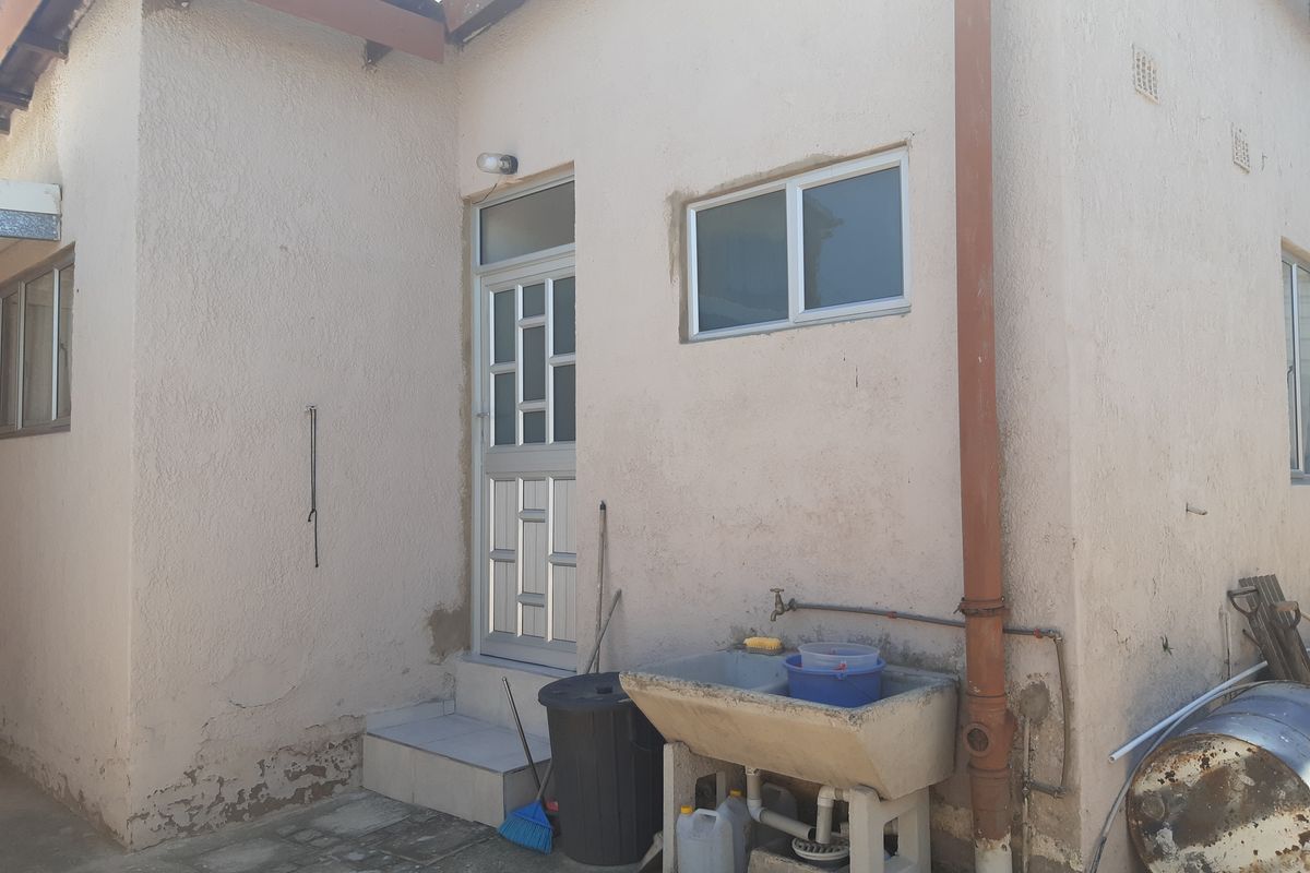 Rear exterior view of the property featuring a utility sink, a single door entrance, and a concrete paved area.