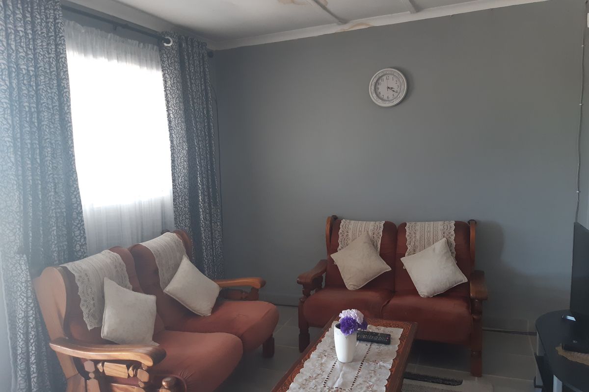 A living room featuring tiled flooring and grey painted walls, with visible water damage on the ceiling.