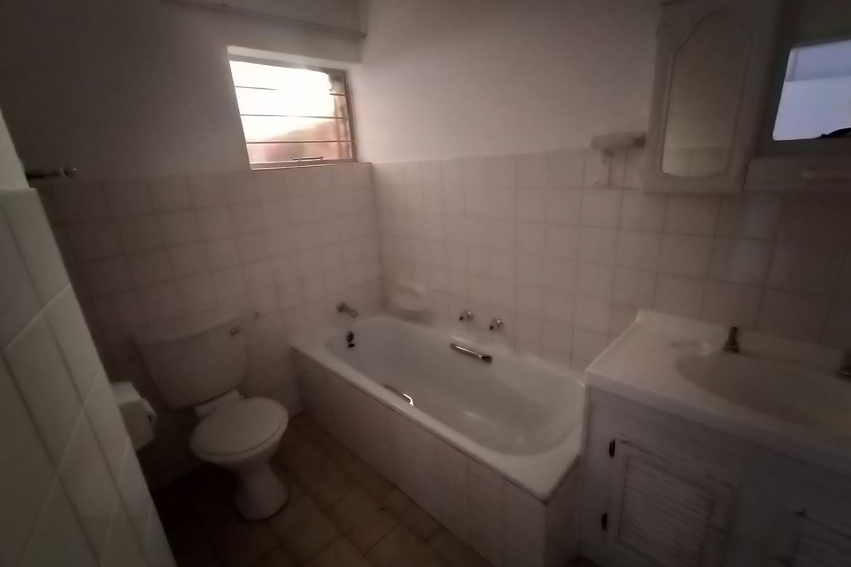 A dated bathroom featuring a built-in vanity, bathtub, and toilet with original wall tiling, offering potential for a modern renovation.