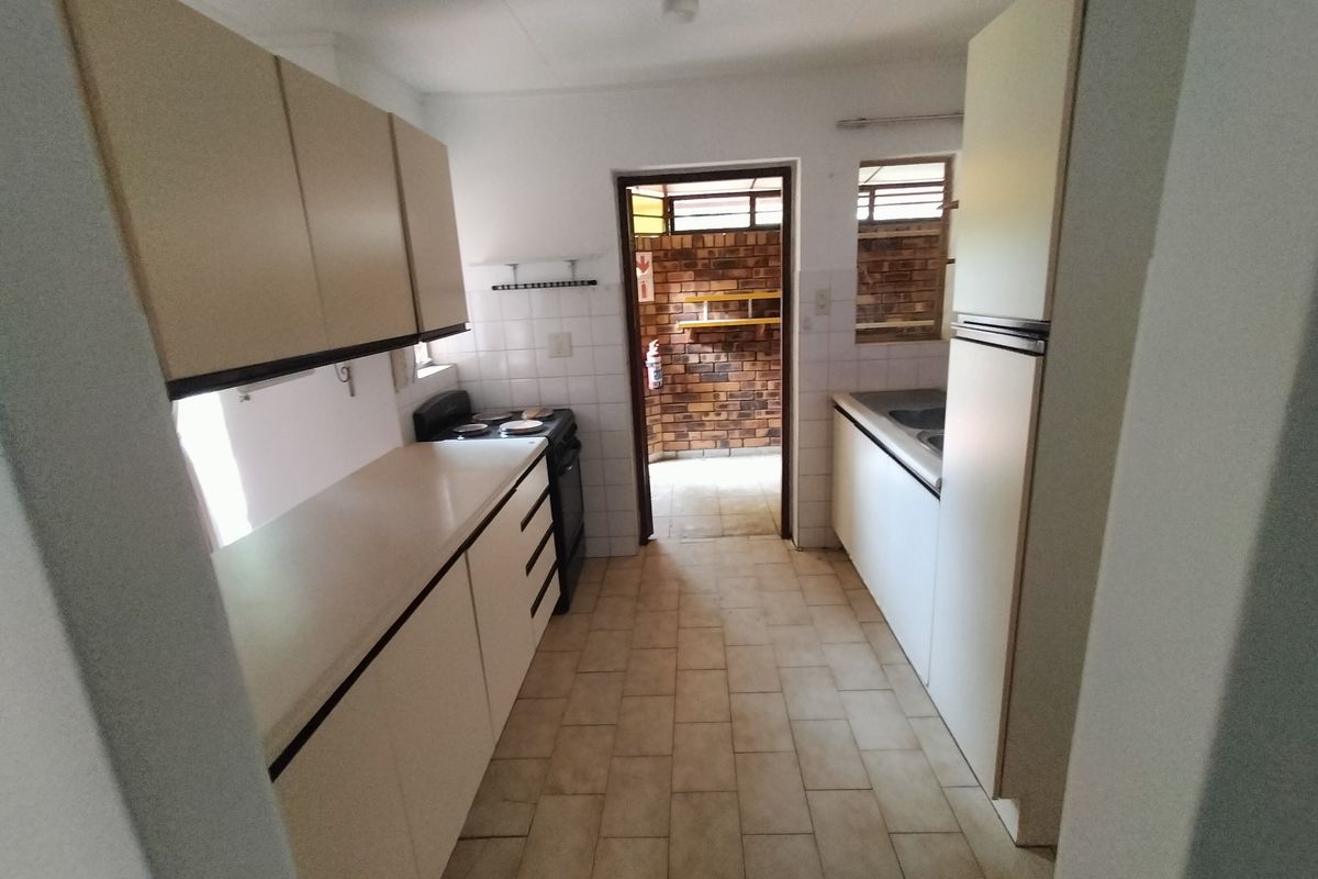 A functional galley-style kitchen featuring laminate cabinetry, tiled flooring, and a built-in stove, offering a practical layout with direct access to an outdoor area.