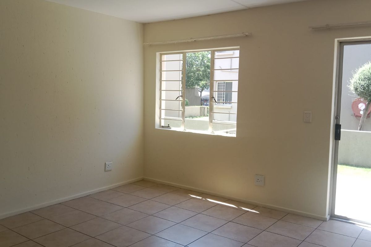 An empty living room featuring tiled flooring, a window with security bars, and a sliding glass door leading to an outdoor area.
