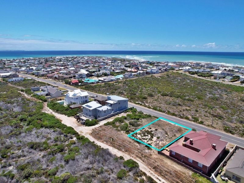 Aerial view of a vacant residential plot situated in a coastal neighborhood, highlighting its proximity to the ocean and surrounding residential development.