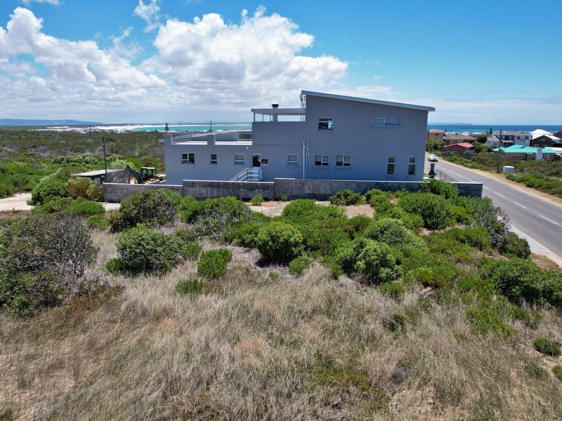 Aerial view of a modern residential property situated on a coastal plot, featuring a flat roof design and surrounding natural vegetation.