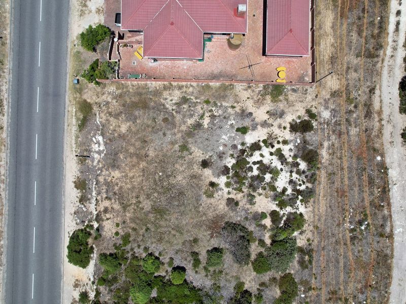 Aerial view of a residential plot featuring a paved area, boundary wall, water tank, and adjacent road access.