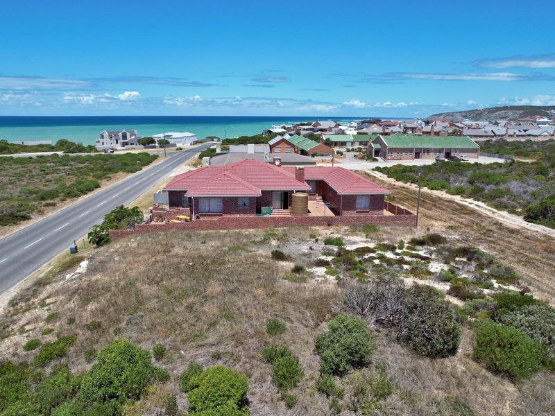 Aerial view of a residential property featuring a brick house with a tiled roof, situated near the coastline with surrounding natural vegetation.