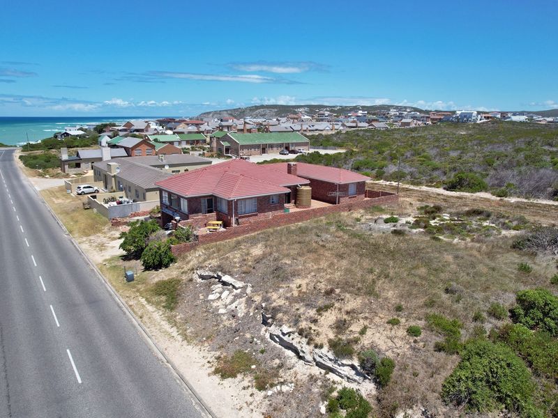 Aerial view of a residential property featuring a brick house with a tiled roof, situated near the coast with surrounding natural vegetation.