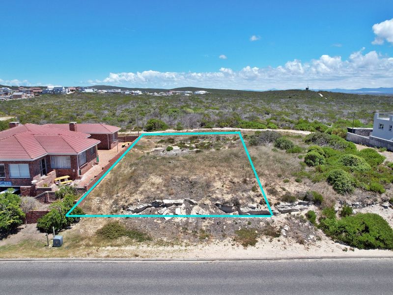 An aerial view of a vacant residential plot with natural vegetation, highlighting the property boundaries in a coastal neighborhood setting.