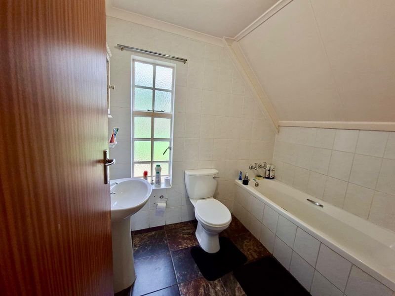 A functional bathroom featuring a pedestal basin, toilet, and bathtub with tiled finishes and a window for natural light.