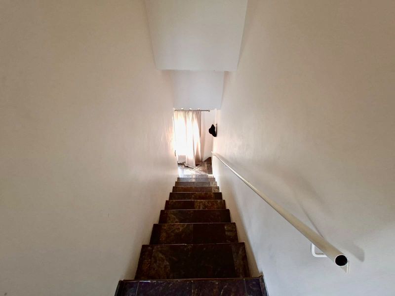 A functional staircase featuring dark tiled steps and a simple white metal handrail, leading down towards a naturally lit landing area.