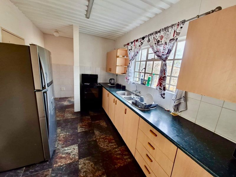 A functional kitchen featuring laminate cabinetry, dark countertops, a double bowl sink, and tiled flooring, offering potential for a modern renovation.