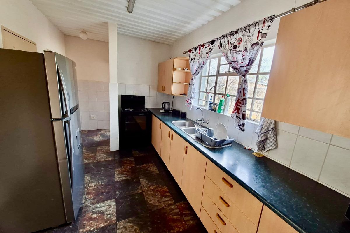 A functional kitchen featuring laminate cabinetry, dark countertops, a double bowl sink, and tiled flooring, offering potential for a modern renovation.