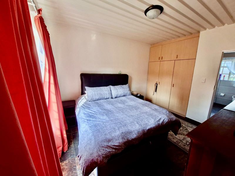 A functional bedroom featuring built-in wooden cupboards, tiled flooring, and direct access to an adjoining bathroom.