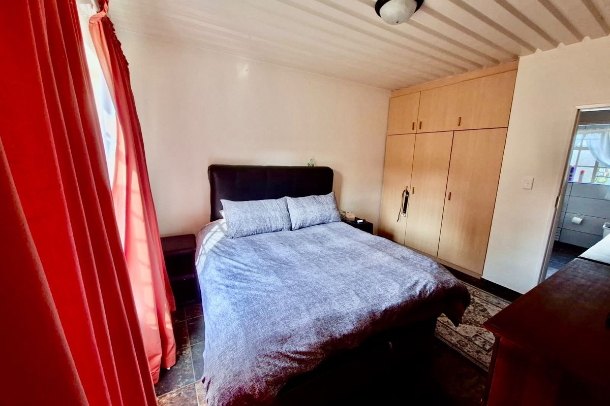 A functional bedroom featuring built-in wooden cupboards, tiled flooring, and direct access to an adjoining bathroom.