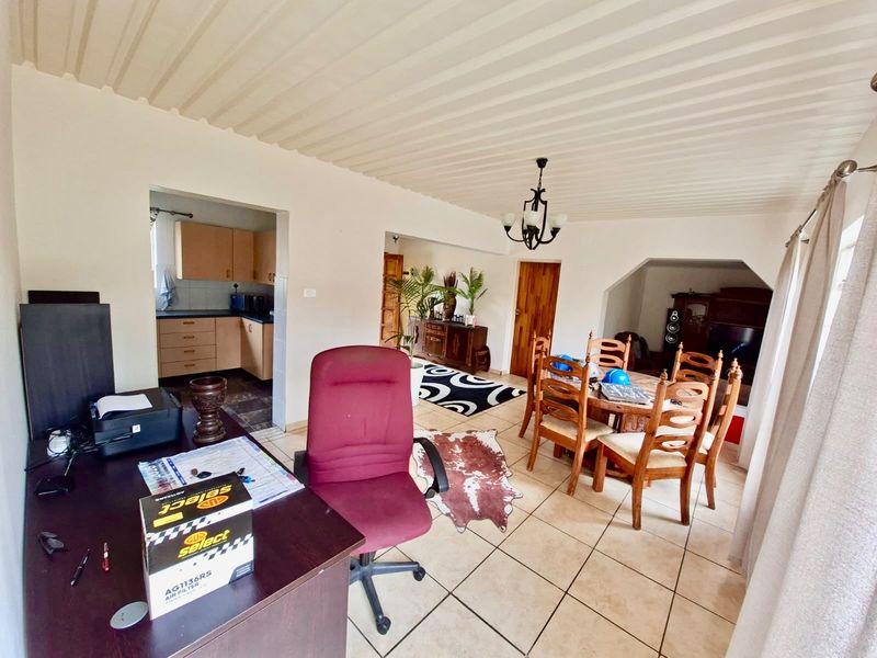 Open plan living and dining area featuring tiled floors, a corrugated ceiling, and an adjacent kitchen with built-in cabinetry.