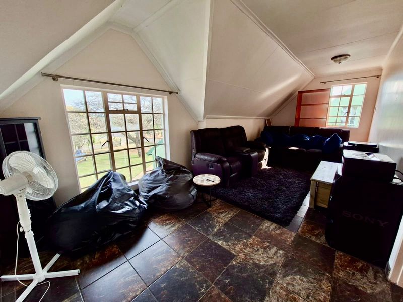 A living room featuring dark tiled flooring, a pitched ceiling, and large windows providing natural light and garden views.