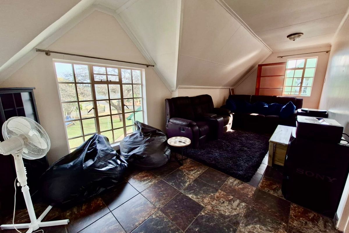 A living room featuring dark tiled flooring, a pitched ceiling, and large windows providing natural light and garden views.