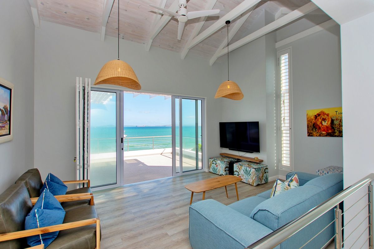 Bright living room featuring vaulted ceilings with exposed rafters, laminate flooring, and large sliding glass doors opening to a scenic ocean-view balcony.