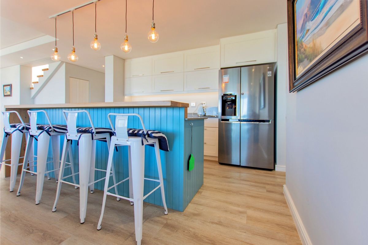 Modern kitchen featuring a vibrant blue island with a breakfast bar, sleek white cabinetry, and contemporary pendant lighting over a light wood-look floor.