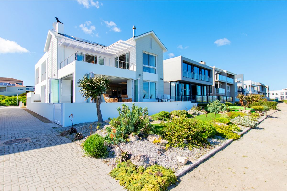 A modern coastal residence featuring a landscaped garden, paved driveway, and an expansive balcony with bi-fold doors opening to the living area.