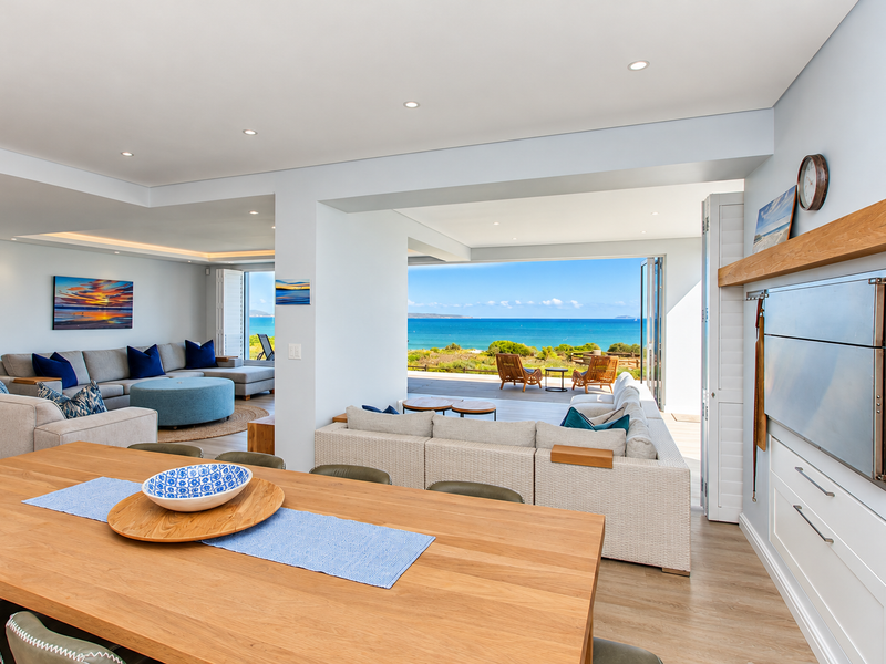 Spacious open-plan living and dining area featuring a built-in braai, modern finishes, and seamless flow to an outdoor patio with panoramic ocean views.