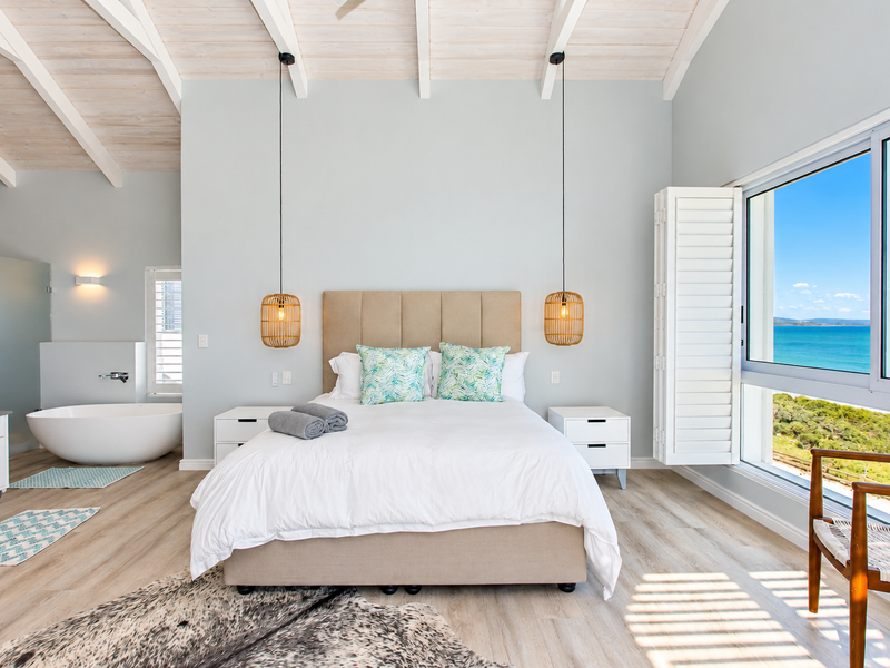Spacious bedroom featuring exposed timber ceiling beams, a luxurious freestanding bathtub, and large windows offering stunning ocean views.
