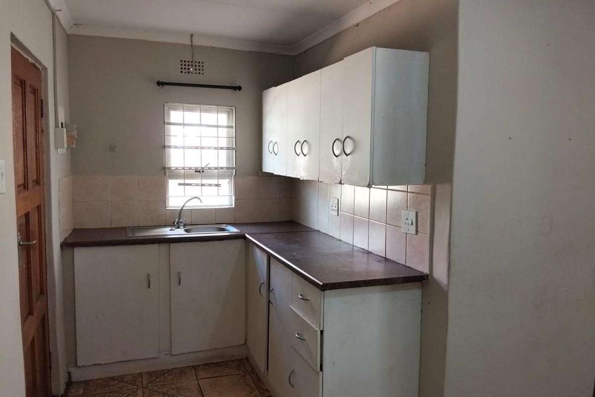 A functional kitchen featuring built-in cabinetry, laminate countertops, a stainless steel sink, and tiled backsplash, offering a blank canvas for renovation.