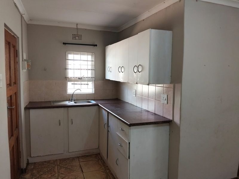 A functional kitchen featuring built-in cabinetry, laminate countertops, a stainless steel sink, and tiled backsplash, offering a blank canvas for renovation.