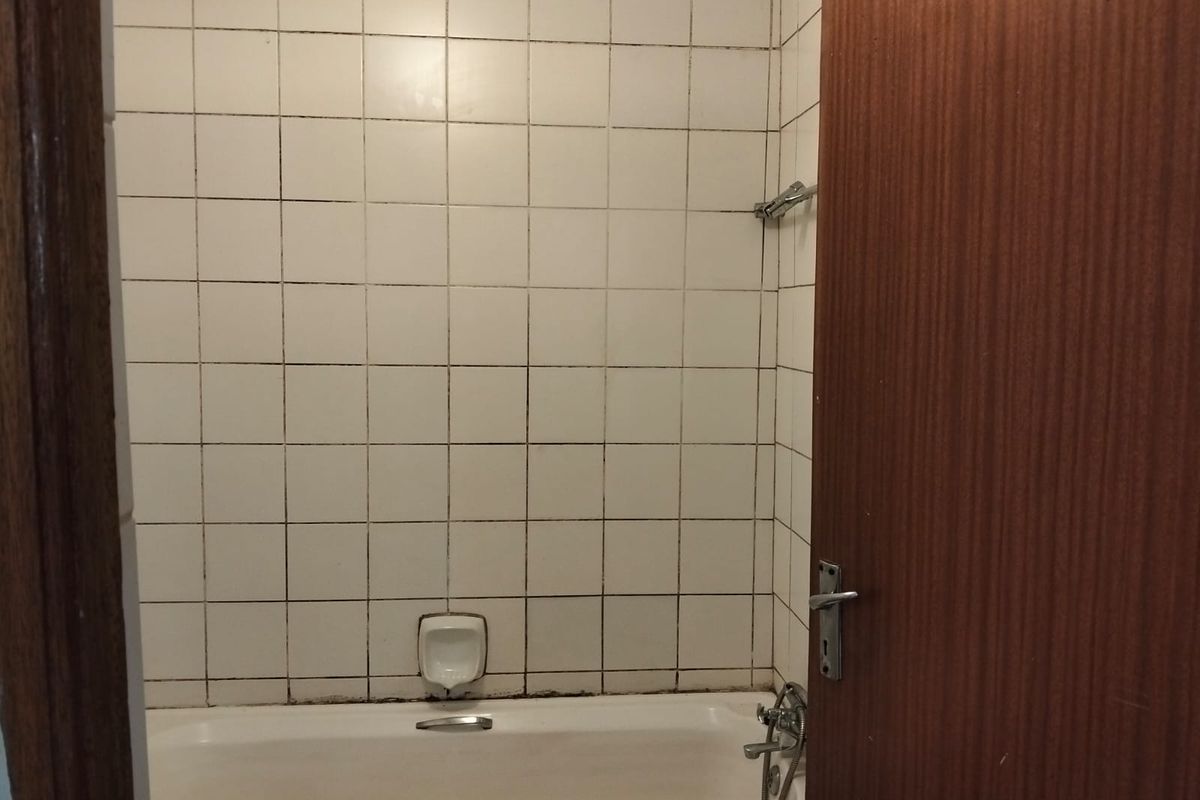 A functional bathroom featuring a standard bathtub with wall-mounted shower mixer and tiled surround, requiring some maintenance to the grout and sealant.