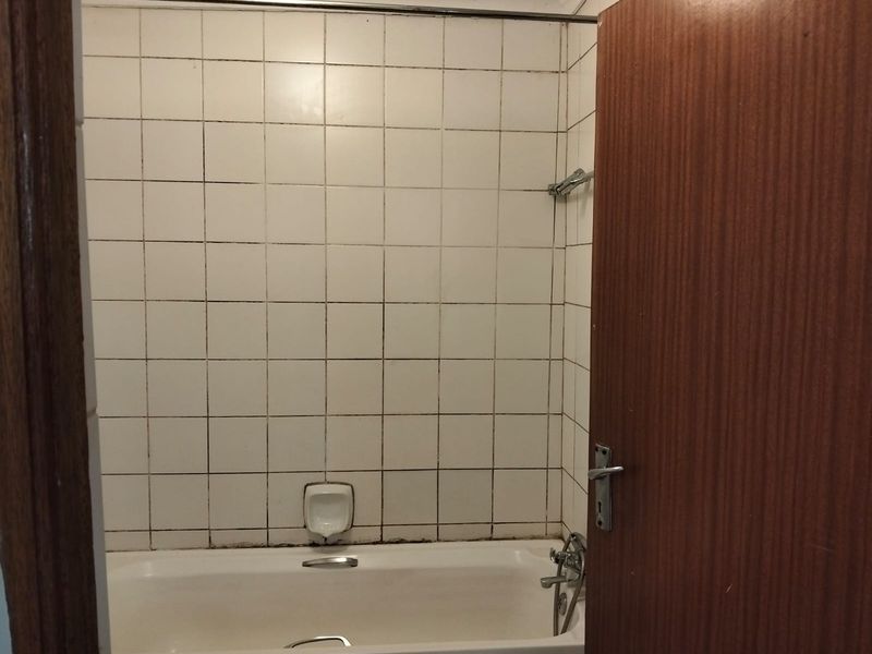 A functional bathroom featuring a standard bathtub with wall-mounted shower mixer and tiled surround, requiring some maintenance to the grout and sealant.
