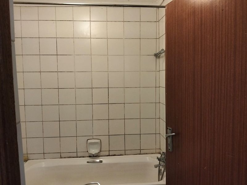 A dated bathroom featuring a built-in bathtub with wall-mounted shower head and tiled surround, requiring cosmetic updates to improve the overall aesthetic.
