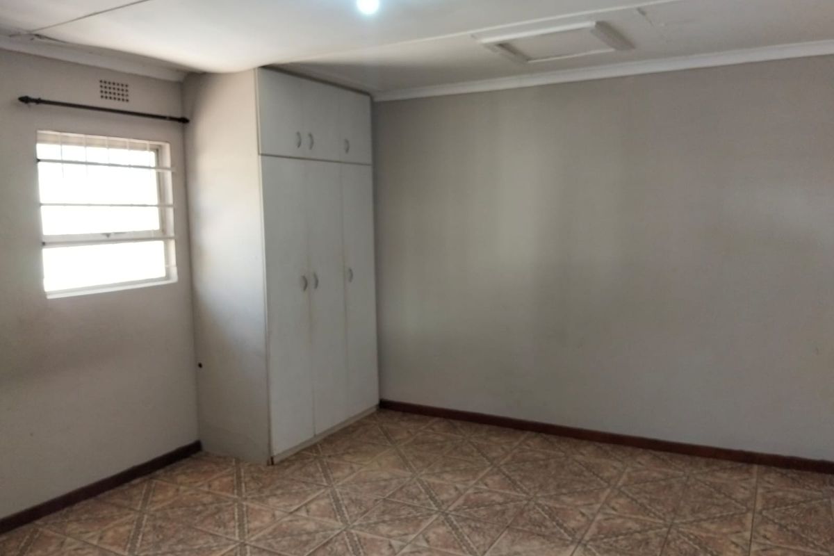 An empty bedroom featuring tiled flooring, a built-in wardrobe, and a window with security bars.