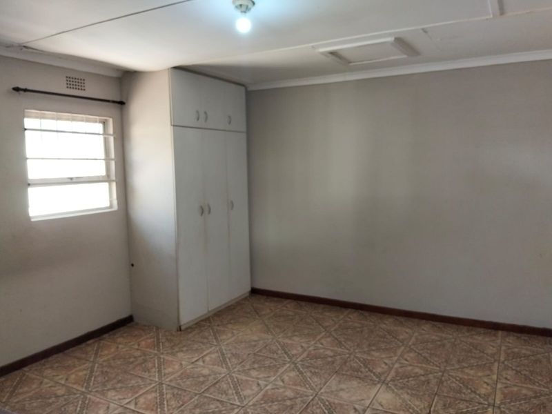 An empty bedroom featuring tiled flooring, a built-in wardrobe, and a window with security bars.