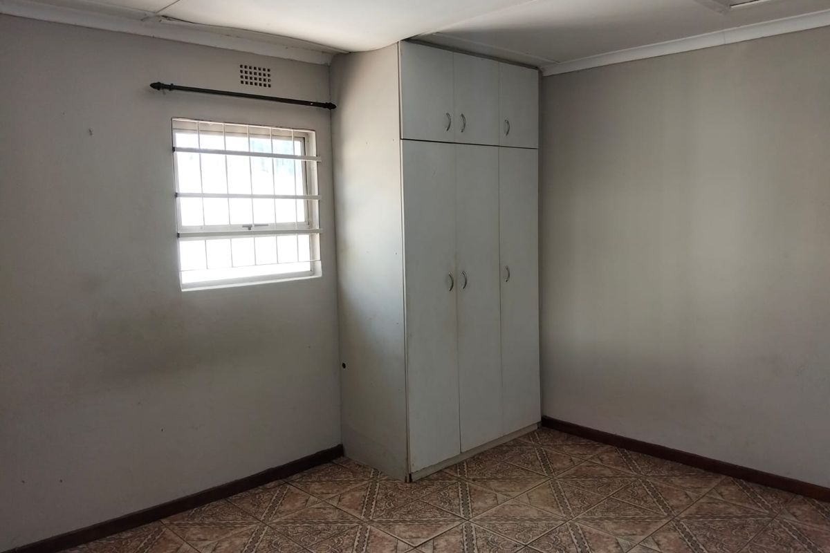 A vacant bedroom featuring built-in cupboards, tiled flooring, and a window fitted with security bars.