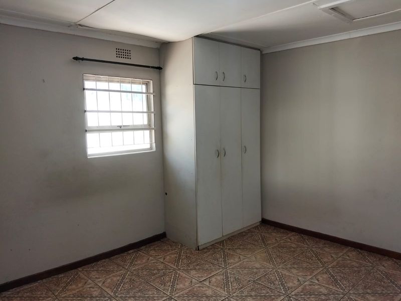 A vacant bedroom featuring built-in cupboards, tiled flooring, and a window fitted with security bars.